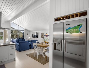 Eine moderne Küche mit einem Edelstahlkühlschrank, eine Essecke mit weißem Tisch und Stühlen sowie eine blaue Sofagarnitur.