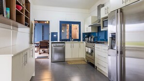 A modern kitchen with stainless steel appliances, white cabinetry, and a blue accent wall. - Bluetongue - Pet Friendly with Spa (Culburra Beach)