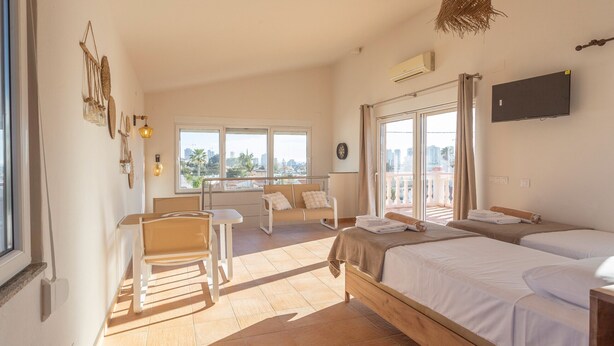 Un dormitorio con cama, una silla, una mesita, un balcón con vistas y un televisor fijado a la pared.