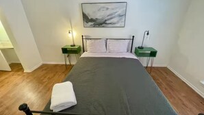 A bedroom with a bed, two bedside tables, a nightstand, a painting on the wall, and a wooden floor. - Charming 2x2 Apt in ATX by UT (Austin)