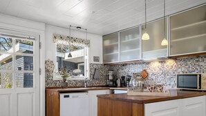 Una cocina moderna con una isla de madera, armarios blancos, lavavajillas, cafetera y microondas.