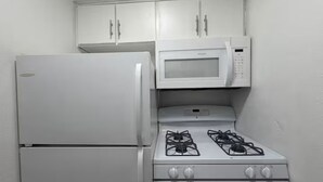 Una cucina compatta con frigorifero bianco, microonde e piano cottura a gas.