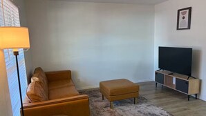 Un soggiorno con divano, poggiapiedi, mobile TV e una lampada.