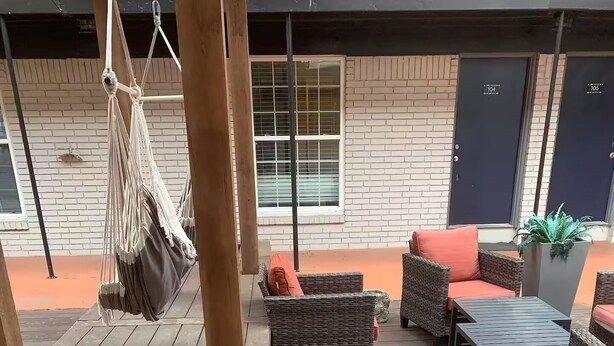 Un terrazzo in legno con mobili in vimini, un'amaca e un vaso con una pianta.