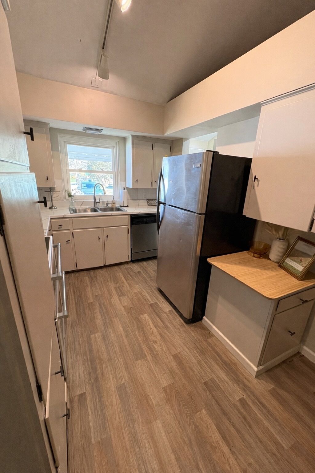 A modern kitchen with a stainless steel refrigerator, wooden countertop, and light-colored cabinets.