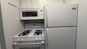 A compact kitchen with a white microwave, gas stove, and refrigerator. - 1x1 Apt Right by Pease Park (Austin)