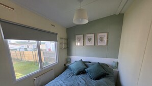 A bedroom with a bed, a window, a radiator, and framed pictures on the wall. - 158 South Happy Days - Sleeps 8 (Skegness)