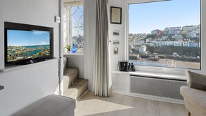 A modern living room with a television, a large window with a city view, a radiator, and a sofa. - Rock Cottage is a charming coastal retreat (Brixham)