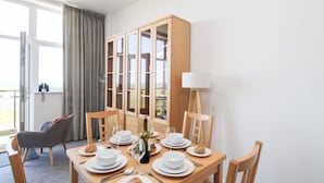 Un coin repas avec une table en bois dressée pour quatre personnes, un meuble avec des portes en verre, une lampe et une vue sur l’extérieur.