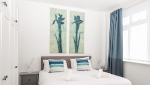 Une chambre à coucher avec un lit, deux oreillers, une table de chevet, un tableau accroché au mur et une fenêtre avec des rideaux.