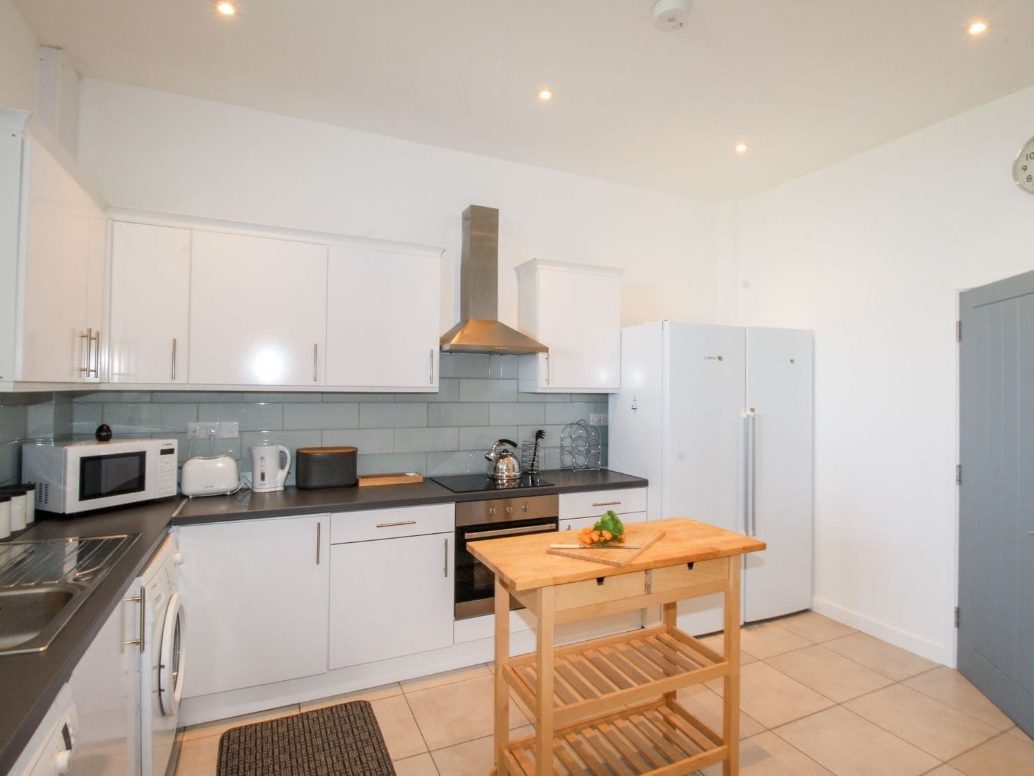 A modern kitchen with white cabinets, a microwave, toaster, kettle, and a refrigerator.
