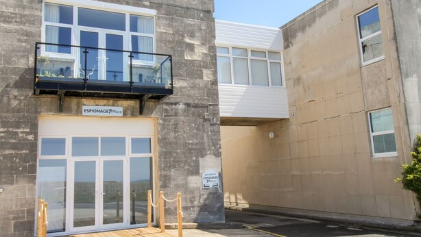 Un immeuble doté d’un balcon, d’une enseigne indiquant « ESPIONNAGE Place » et d’une terrasse en bois.