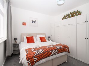 Un dormitorio con cama, mesita de noche, armario y una obra de arte colgada en la pared.