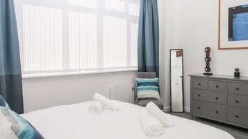 A hotel room with a bed, a dresser, a radiator, a window with curtains, and a framed picture on the wall.