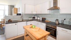 Une cuisine moderne avec des armoires blanches, une hotte de cuisinière en acier inoxydable, un four à micro-ondes encastré et un lave-vaisselle.