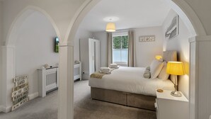 Une chambre à coucher avec un grand lit, une table de chevet avec une lampe, un radiateur et une fenêtre avec des rideaux.