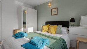 A neatly made bed with rolled towels, a bedside table with a lamp, and a television on a stand. - Prime central location at Harbour Heights in Brixham (Brixham)