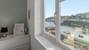 A room with a large window overlooking a harbor, a lamp, and a framed picture on the dresser. - Prime central location at Harbour Heights in Brixham (Brixham)