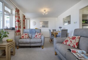 A living room with two grey sofas, a wooden table, a clock, and a window with curtains. - Enjoy a relaxing seaside escape at Ocean Side Apartment (Brixham)