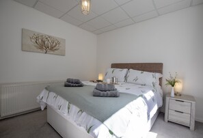 Un dormitorio con cama, mesitas de noche, un radiador, una lámpara de pared y un cuadro.
