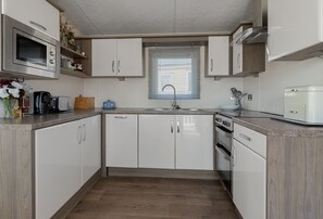 A compact kitchen with white cabinets, a built-in oven, a microwave, and a sink.