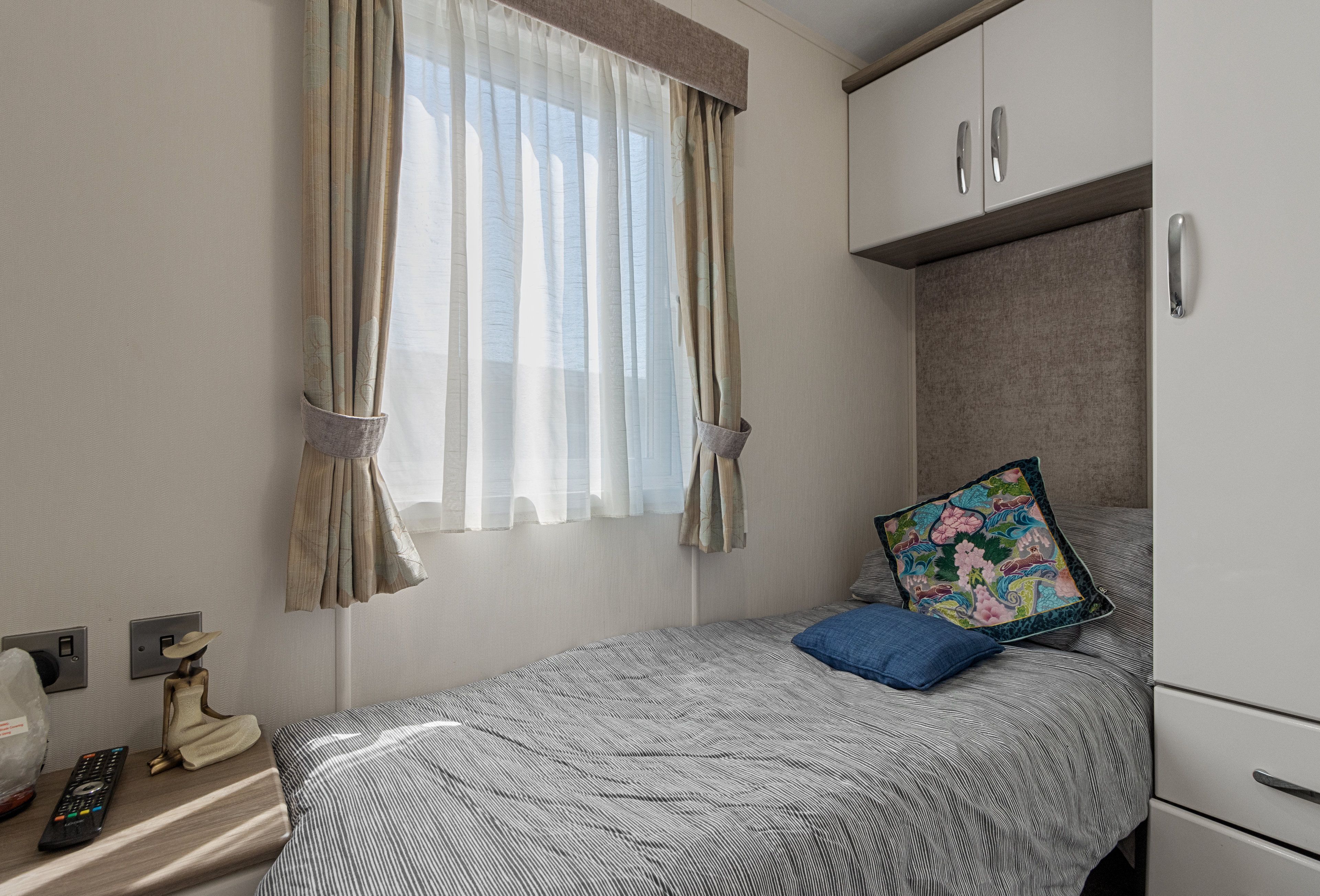 A bedroom with a bed, a nightstand, a remote control, a decorative item, and a window with curtains.