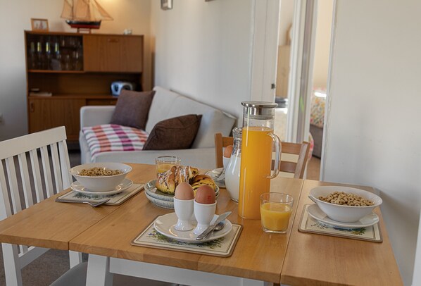 Une table de petit-déjeuner avec des bols de céréales, des œufs, une carafe de jus d’orange et une cafetière.