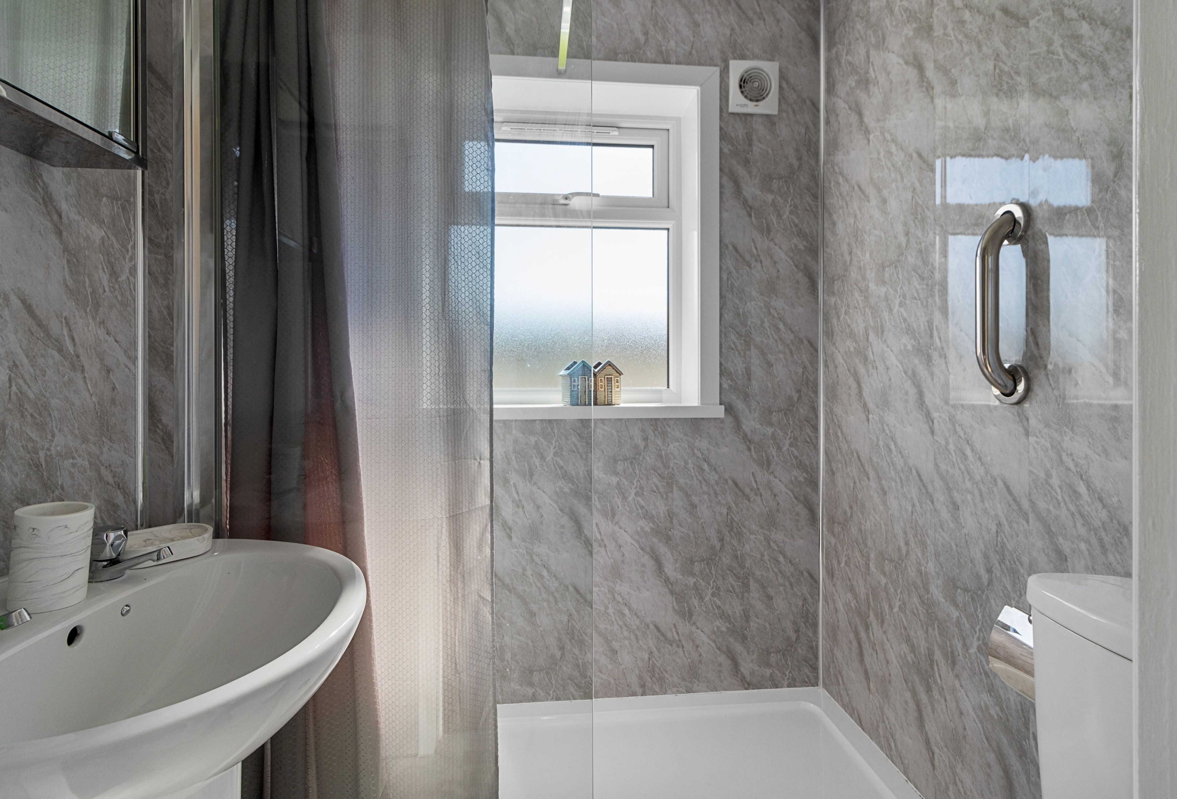 Un baño con lavamanos, ventana, ducha e inodoro.