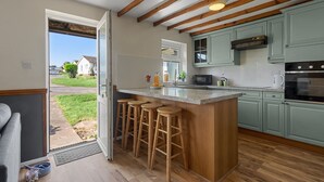 A kitchen with wooden beams, a bar stool area, and a view through an open door. - Landscove Chalet 19 a charming and cosy South Devon holiday cottage (Brixham)