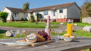A picnic setup with food and drinks on a wooden table, a house with a red roof in the background. - Landscove Chalet 19 a charming and cosy South Devon holiday cottage (Brixham)