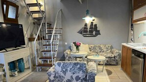 Ein Wohnzimmer mit einer Couch, einem Couchtisch, einem Fernseher, einer Treppe und einer Küchenzeile.