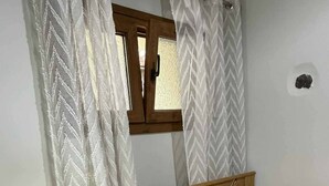 Ein kleines Schlafzimmer mit einem hölzernen Bett, einem Schreibtisch mit Lampe und einem Fenster mit Holzrahmen.