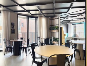A modern interior with a round table, black chairs, a plant shelf, and large windows. - Nik Vila Mariana (São Paulo)