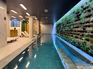 A swimming pool with a long, narrow design, surrounded by lounge chairs and a wall with vertical gardens. - Nik Vila Mariana (São Paulo)