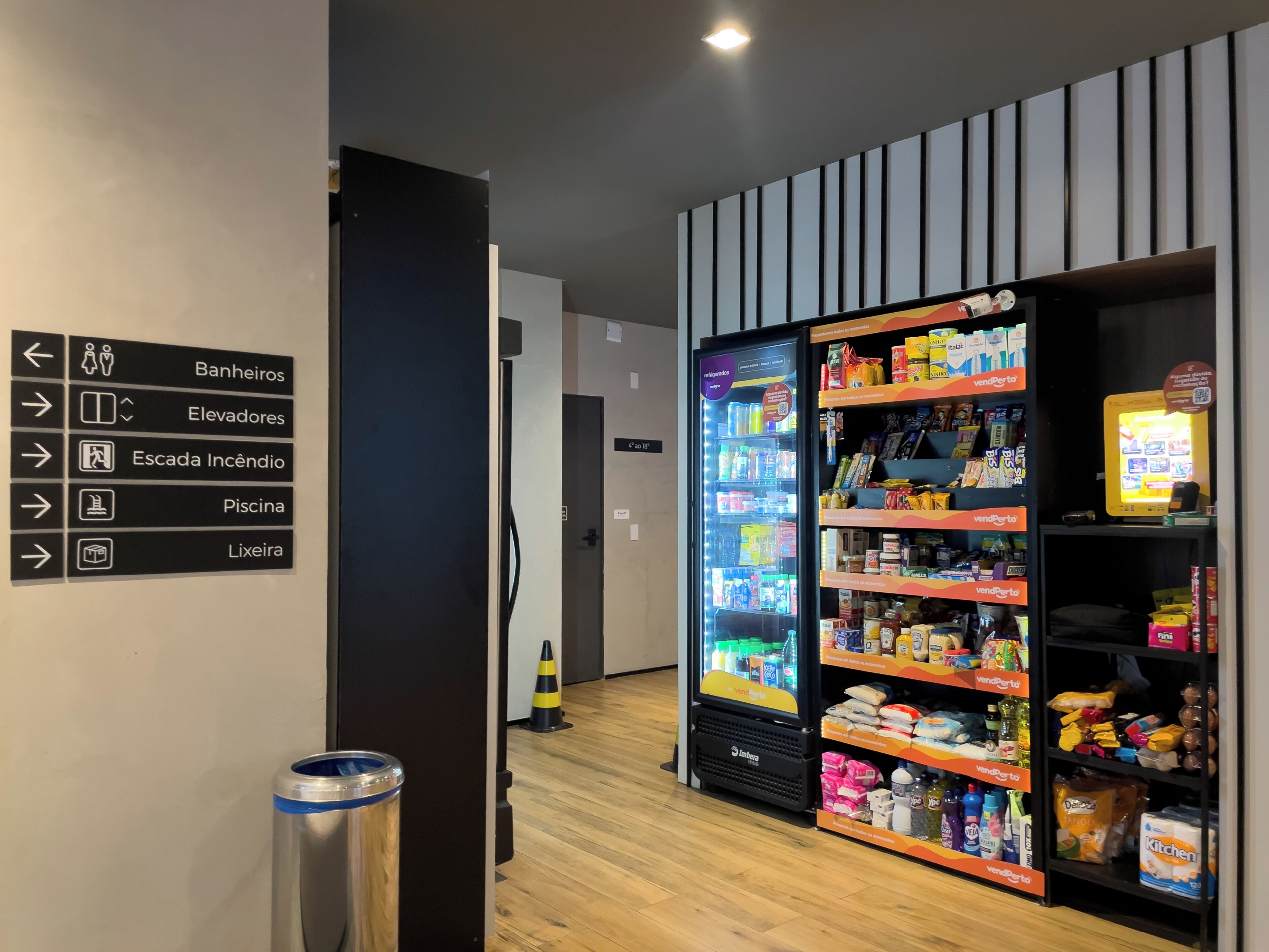 A hotel corridor with directional signs, a vending machine, and a trash bin.