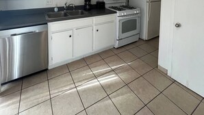 Ett kök med vita skåp, en diskmaskin i rostfritt stål, en mikrovågsugn, en spis och ett kylskåp.