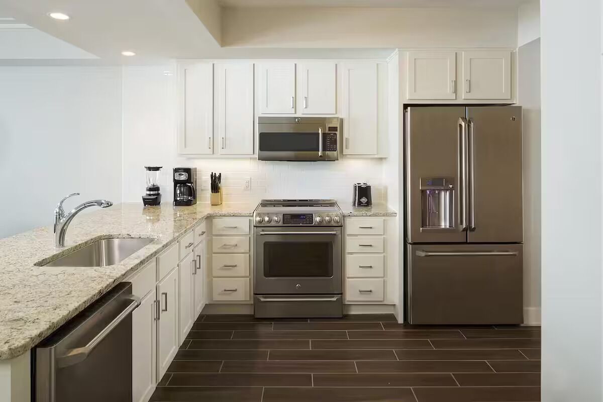 Une cuisine moderne avec des armoires blanches, des appareils électroménagers en acier inoxydable, un comptoir en granit et un lave-vaisselle.
