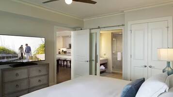 Une chambre d’hôtel équipée d’un lit, d’une télévision, d’un ventilateur de plafond, d’une salle de bain avec un miroir et d’une porte donnant sur un coin cuisine.