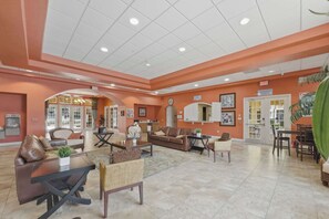 A spacious lobby with a large seating area, a kitchen in the background, and a dining area with a green curtain. - Cozy Disney Getaway 2BR  5 Mins to Parks (Kissimmee)