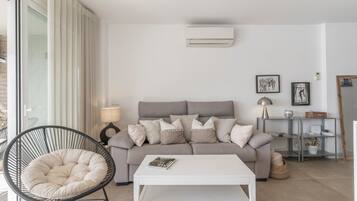 Una sala de estar moderna con un sofá gris, una mesa de centro blanca, una silla de mimbre negra y una lámpara blanca.