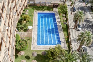 Une piscine dotée d’une terrasse carrelée, entourée de palmiers et bordée d’un bâtiment au design architectural unique.