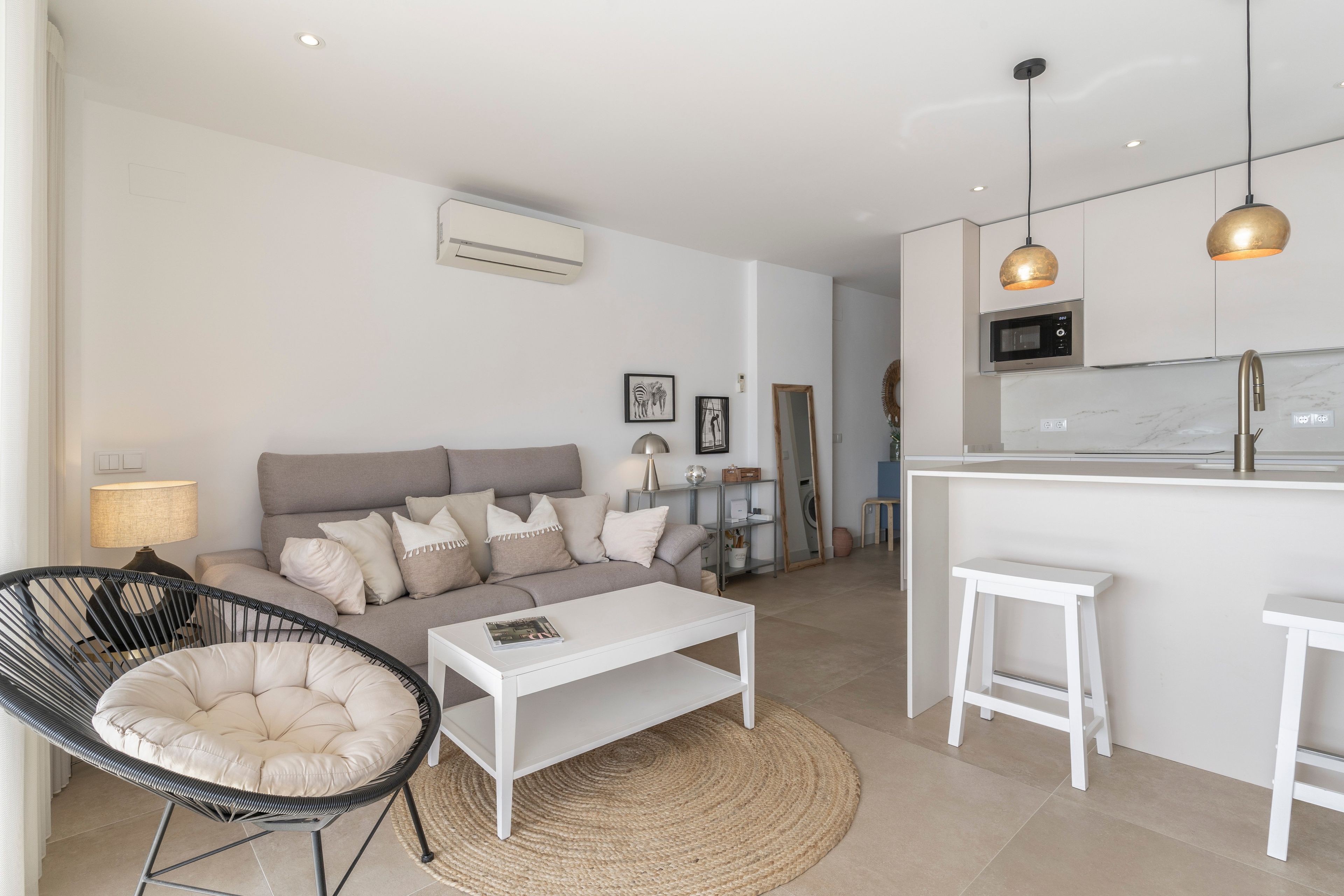 A modern living room with a sofa, coffee table, and a chair. There is a kitchen area with a microwave and a sink.