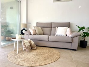 Un saló modern amb un sofà gris, una catifa rodona teixida, una taula auxiliar petita blanca amb espelmes i una planta en test.
