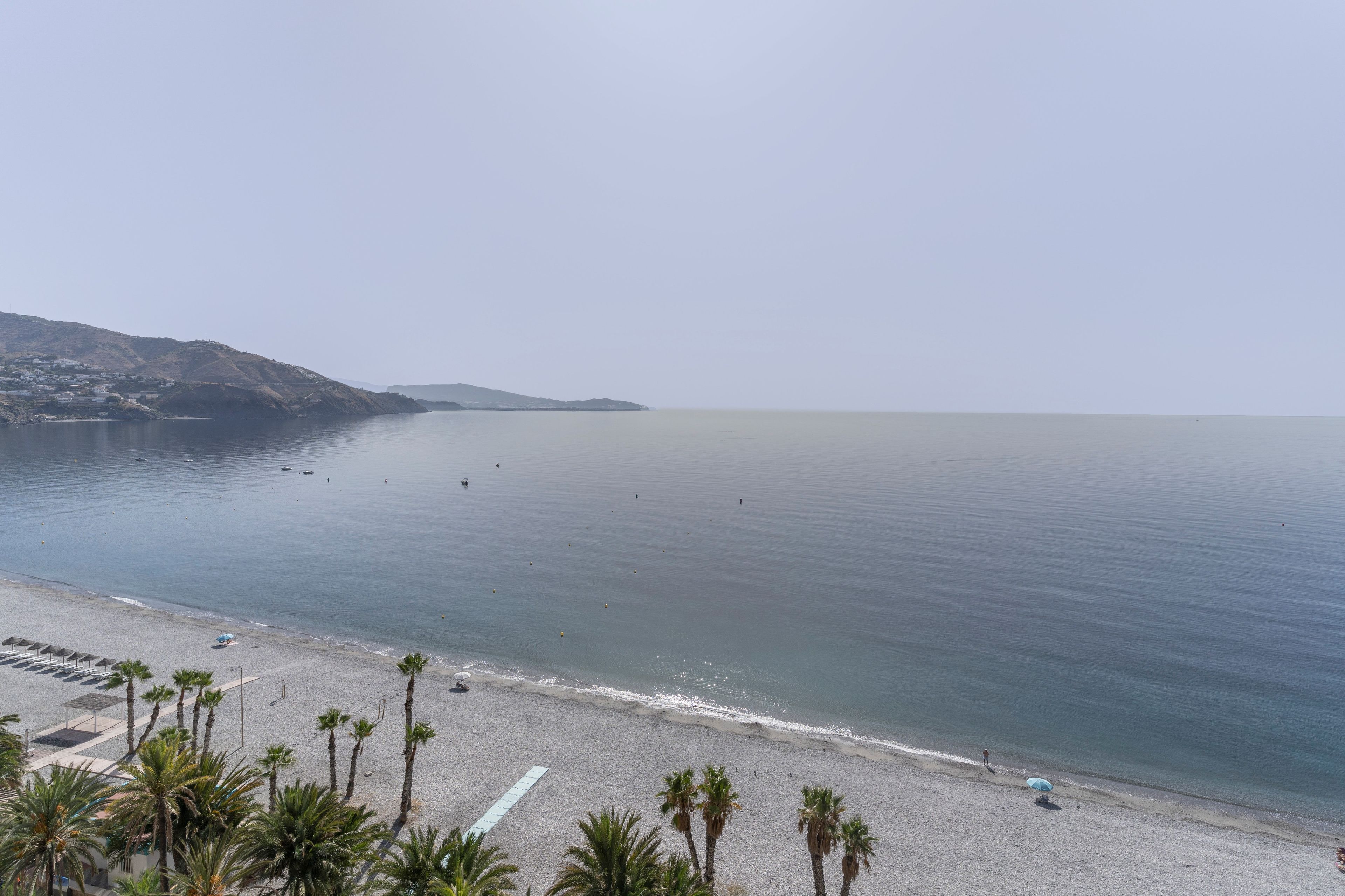 Una playa con cielo despejado, mar tranquilo y algunas personas.