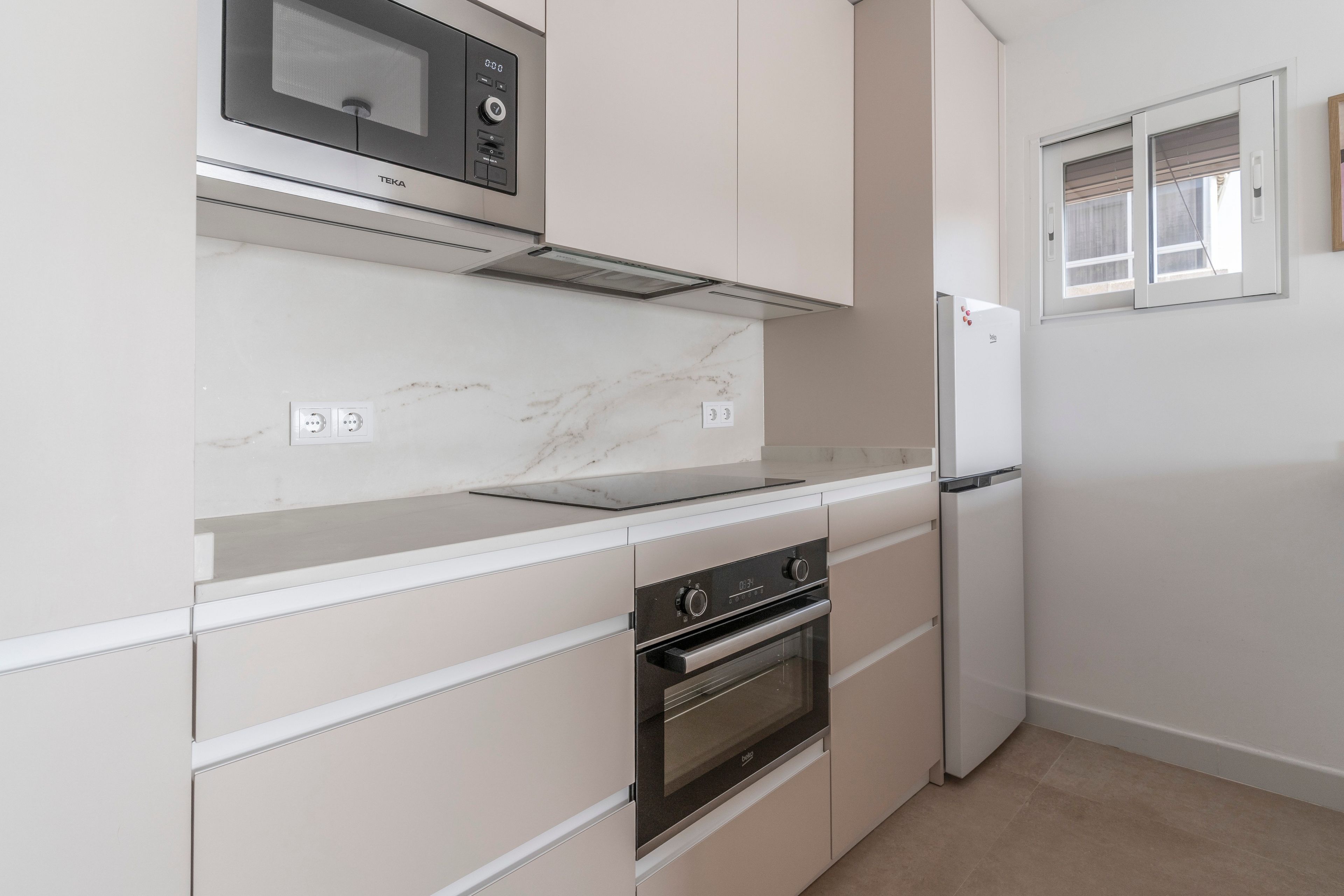 Una cocina equipada con microondas, horno y refrigerador. Hay dos tomas de corriente en la encimera.