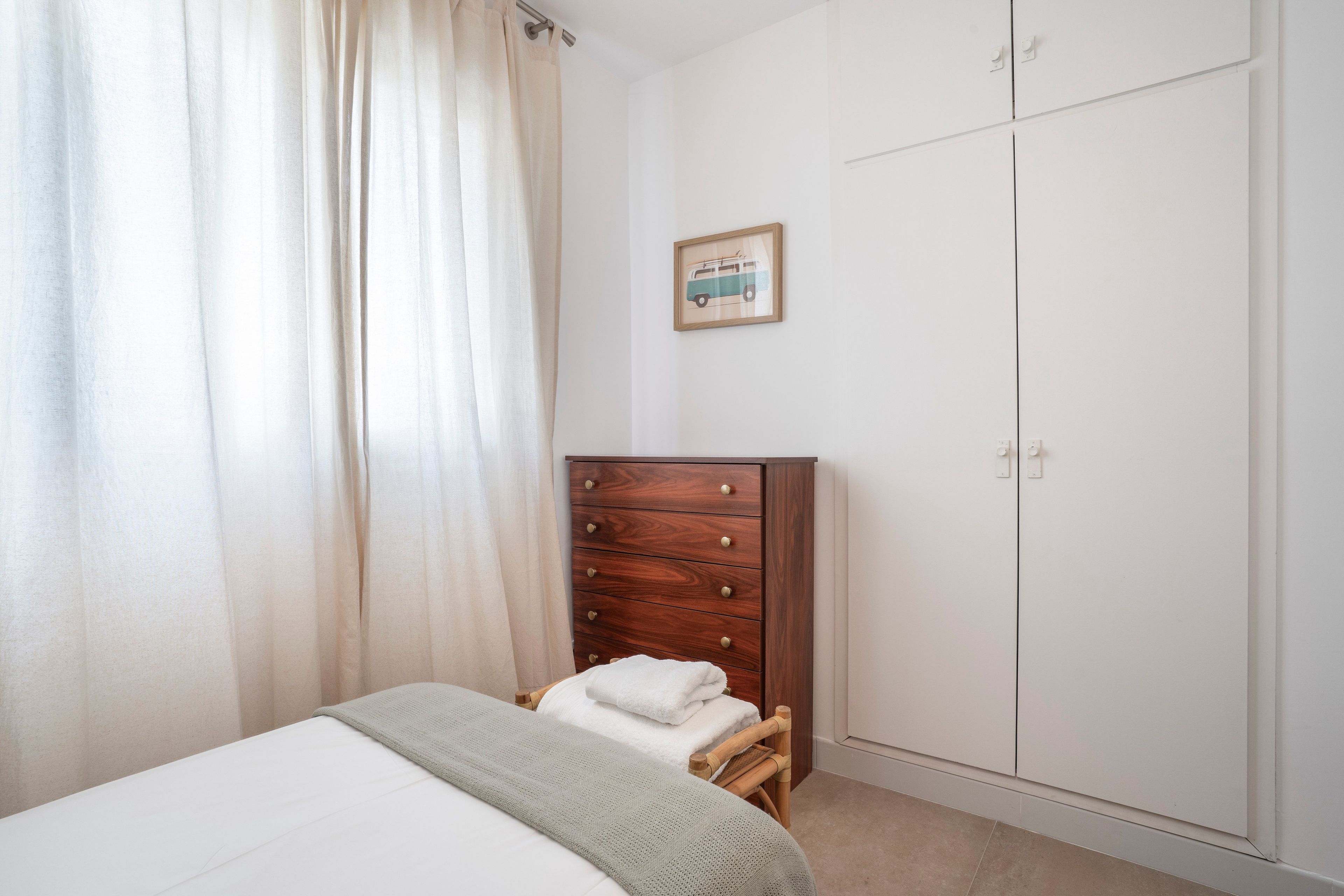 Un dormitorio con una cama, un aparador de madera, un armario y un cuadro en la pared.