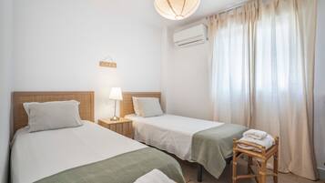 A room with two single beds, a bedside table with a lamp, a 'LOVE' sign, an air conditioning unit, and a window with curtains.