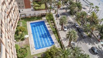 Una piscina en la azotea con superficie de agua azul cristalina, rodeada de palmeras y un aparcamiento.