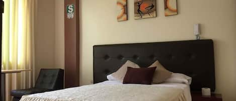 A hotel room with a large bed, a chair, a nightstand, and wall art.