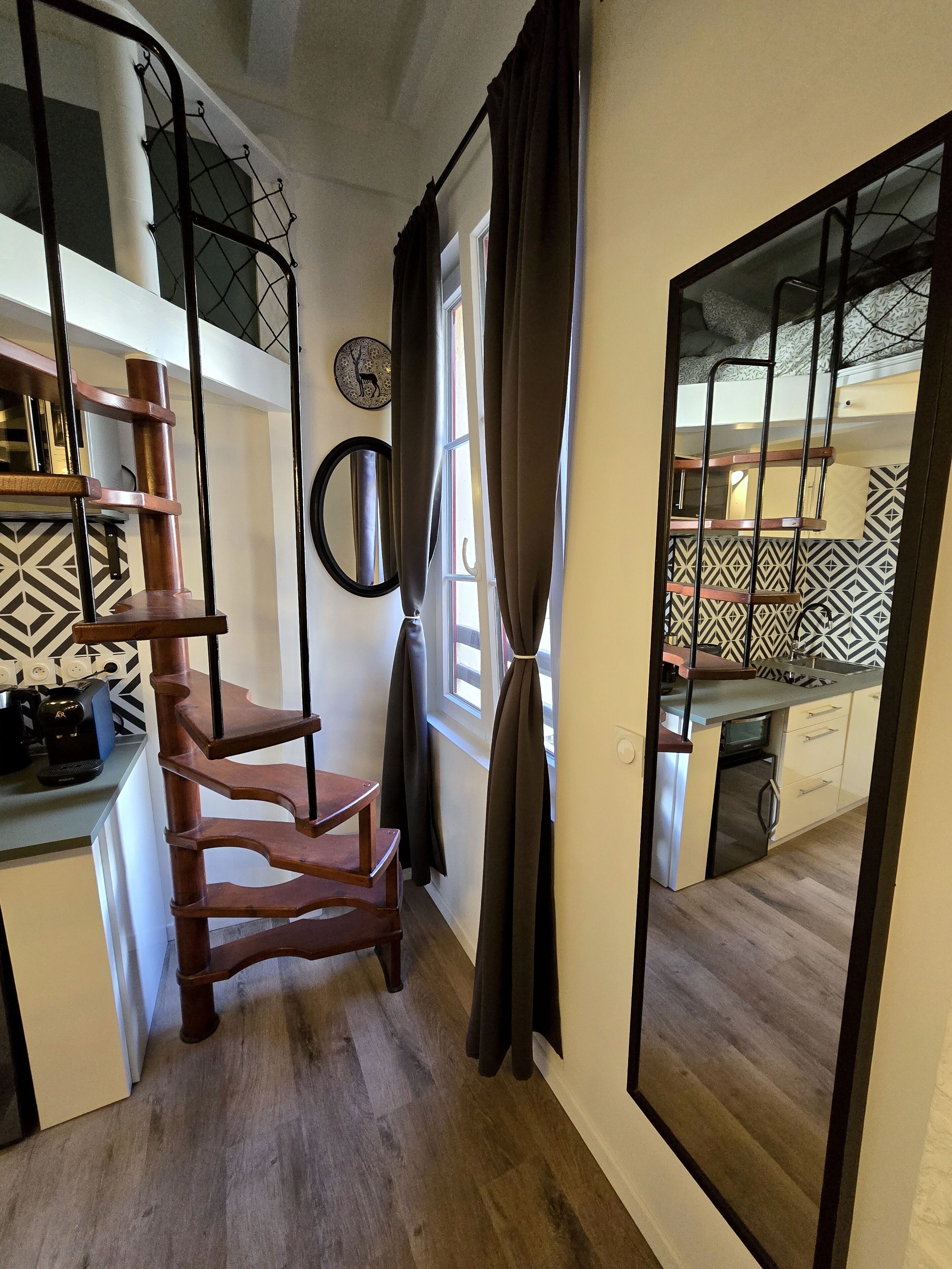 A modern interior with a wooden staircase, a kitchen area, and a view through a glass door.